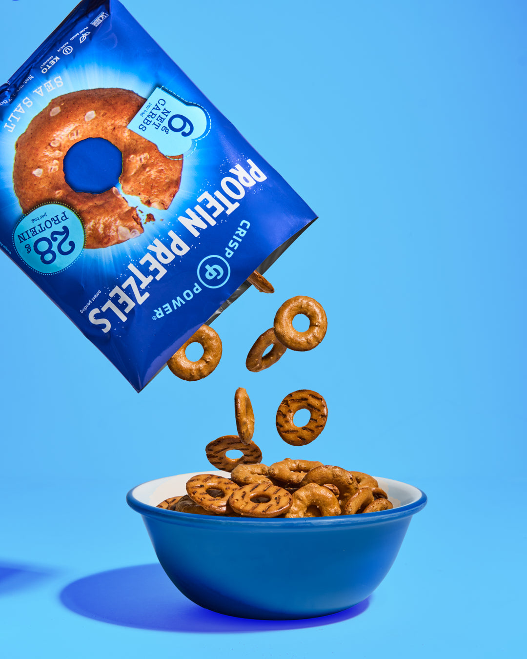 Protein pretzels spilling out of a blue box onto a bowl against a blue background